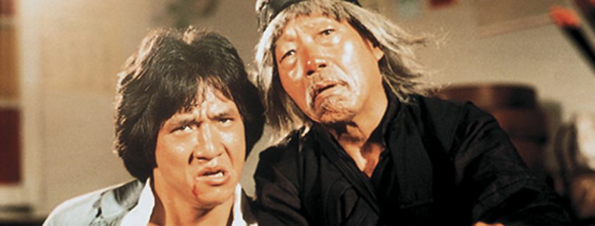 A imagem mostra Jackie Chan e o ator Yuen Siu-tien em uma cena do filme de 1978, "O Mestre Invencível". Eles estão próximos um do outro, com expressões faciais sérias.