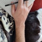 páginas matinais com meu gato Foto de uma mão segurando lápis, com uma folha embaixo, e um gato deitado ao lado da pessoa que está escrevendo.