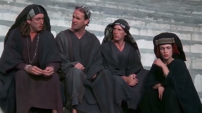 A imagem mostra uma cena do filme "A Vida de Brian". Quatro pessoas, três homens e uma mulher, estão sentadas em degraus de pedra. Todos estão vestidos com túnicas escuras e coberturas para a cabeça, com expressões pensativas.