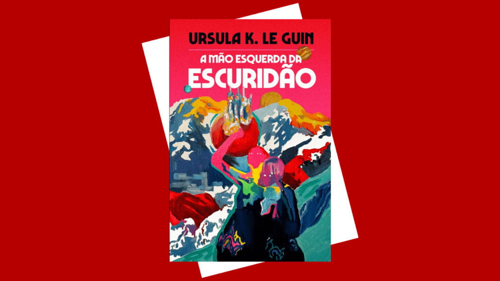 Capa do livro A Mão Esquerda da Escuridão, de Ursula K. Le Guin, sobre fundo vermelho. A ilustração mostra uma figura humana estilizada, de costas, caminhando em uma paisagem montanhosa e gelada, com cores vibrantes como rosa, azul, verde e amarelo. No topo, lê-se o nome da autora “Ursula K. Le Guin” e o título “A Mão Esquerda da Escuridão”. A imagem sugere um cenário alienígena, frio e simbólico, ligado à ficção científica.