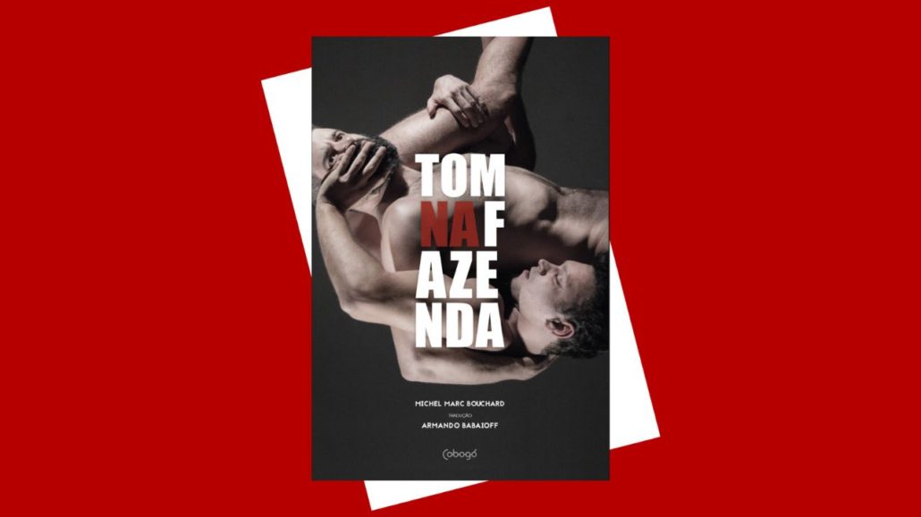 Capa do livro Tom na Fazenda. Dois homens estão entrelaçados em uma pose tensa, com os corpos inclinados e próximos. O título aparece em letras grandes, com “NA” em vermelho e o restante em branco, sobre fundo escuro.