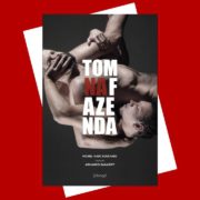Capa do livro Tom na Fazenda. Dois homens estão entrelaçados em uma pose tensa, com os corpos inclinados e próximos. O título aparece em letras grandes, com “NA” em vermelho e o restante em branco, sobre fundo escuro.